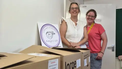 Two women standing next to cardboard boxes stacked against a wall