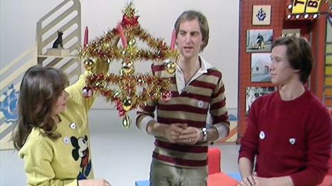 The Blue Peter presenters looking at the tinsel-wrapped Advent crown, which has a wonky candle.