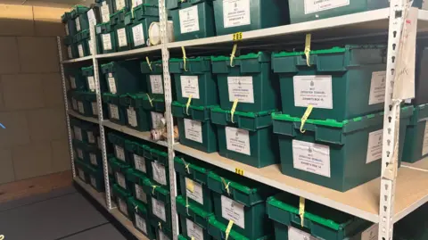 Avon and Somerset Police Dozens of green boxes are stacked on shelves.