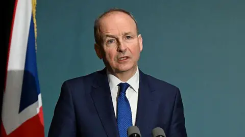Getty Images Micheál Martin speaking into a microphone. He is wearing a navy suit, white shirt and a blue tie.