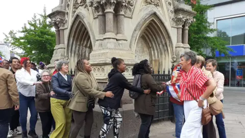 A line of a dozen people dancing with the Clock Tower in the background