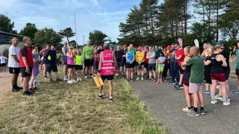 Alice Harvey A Parkrun volunteer wearing a pink high-vis speaks to a crowd of people about to take part in the event in Jersey.