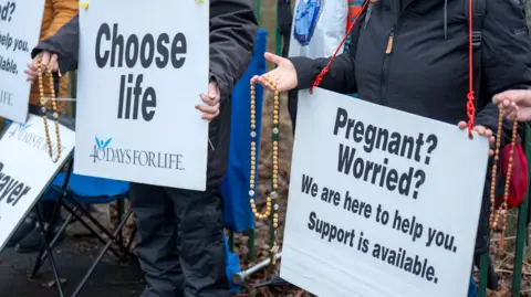 People with their faces hidden holding placards displaying anti-abortion messages.
