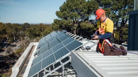 Stock image of a man installing solar panels on a roof