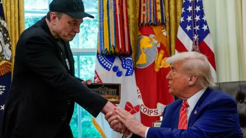 Musk and Trump shaking hands in the White House last week as Trump hands Musk a golden key