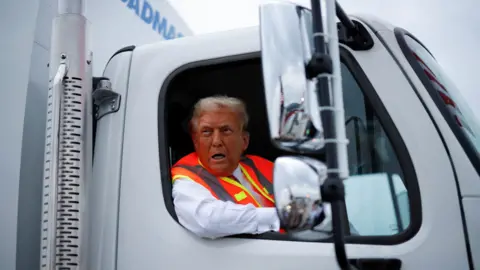 Trump leaning out window of a garbage truck.