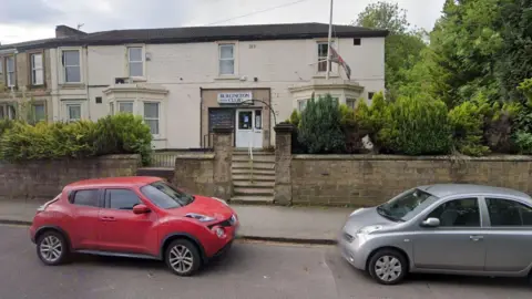 A social club which looks like a 1930s building painted cream, with a sign that reads 'Burlington Club' and a union flag is flying 