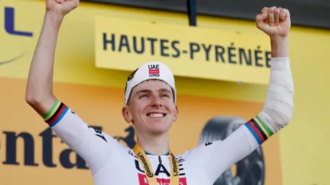 Tadej Pogacar with his arms aloft on the podium after winning stage 12 of the 2025 Tour de France
