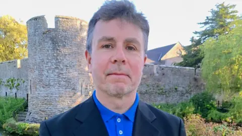 Peter Welsh Peter Welsh standing in front of a stone castle-shaped structure.