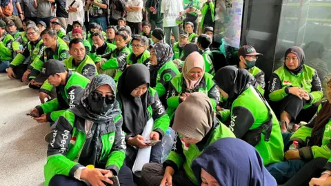 BBC/Liza Tambunan Gojek drivers wearing green uniforms seated outside a Jakarta courthouse where a verdict in the corruption case against the app's founder Nadiem Makarim is being delivered.