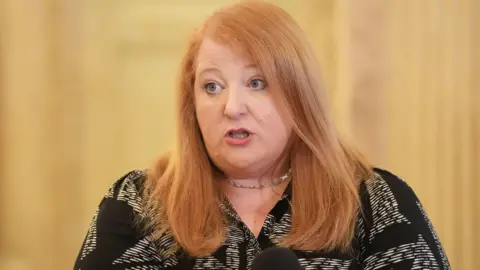 PA Media Naomi Long has long red hair and is wearing a black and white top.