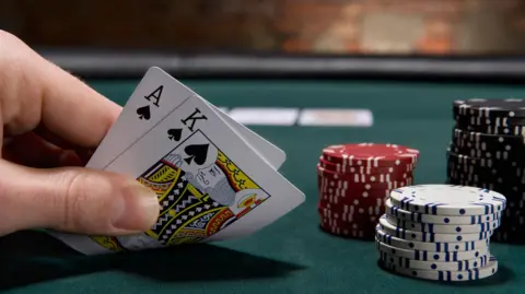 Getty Images A hand holding to poker cards - an ace and a king - next to a pile of poker chips