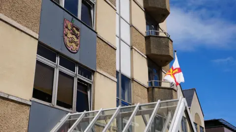 BBC Frossard House - A building with the States of Guernsey logo and a Guernsey flag flying outside it. 