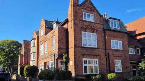 A large red-brick building with large white-framed windows.