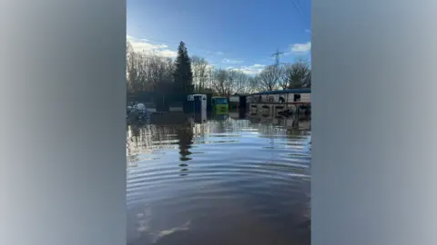 Sarah Reilly Floodwater in a field, with a van in the background and other farming equipment, submerged in water