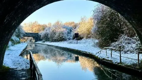 BBC Weather Watchers/Early Bird A view from underneath a canal bridge of a canal with snow covering the towpaths on either side and trees on the far side
