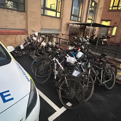 Leicester City Police Seized e-scooters and e-bikes are pictured piled next to a police car