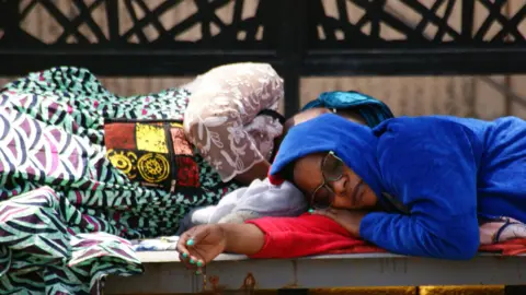  Peter Njoroge/BBC Two female passengers sleep at JKIA airport amid widespread disruption