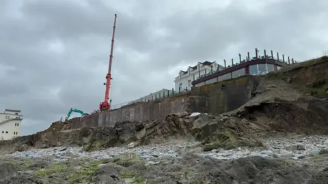 The view from the beach of the new wall under construction in front of the bar and restaurant with a large red crane to the left.