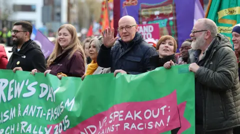 PA Media John Swinney at an anti-racism rally - he is one of several people holding a large green banner that reads "stand up, speak out against racism".