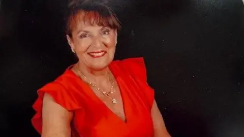 Woman in red blouse with brown hair tied back brown fringe sat smiling against black professional background