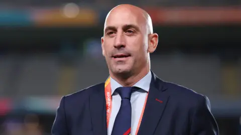 Getty Images Luis Rubiales, wearing a suit, tie and lanyard, looks on in a football stadium