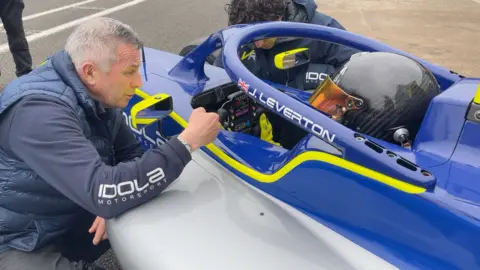 Jamie is sitting in his GB4 car with Steve coaching him from outside the cockpit.