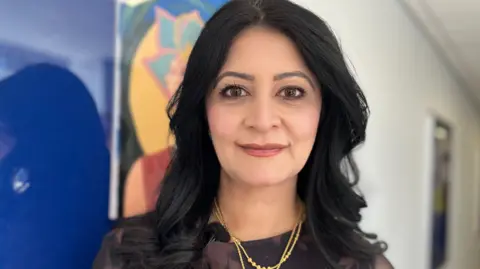 Emma Baugh/BBC Shabina, a woman with long black hair, smiling for camera. 