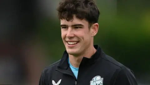 Getty Images Late cricketer Josh Baker, a young man with dark curly hair, smiles while looking off-camera. He is wearing a black Worcestershire Rapids top.