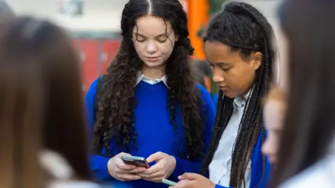 Getty image stock image is the image of two female school children who sees their phone in school