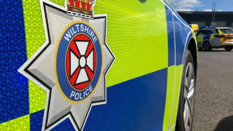 A close-up image of a yellow and blue Wiltshire Police car bearing the Wiltshire Police crest.