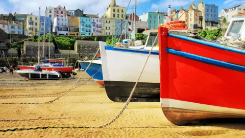 Getty Images Colourful fishing boats moored up on the beach in Tenby at low tide. Colouful houses and buildings line the coast