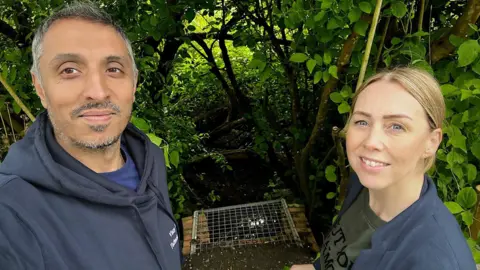 Leanne Stevenson/Vinay Manro Vinay Manro (left) and Leanne Stevenson (right) stand in front of the newly grated culvert, which is in the middle of them in the picture. They both smile at the camera.
