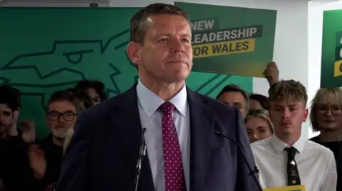 PA Media Rhun ap Iorwerth speaking after the results at the count in Llandudno, surrounded by party supporters