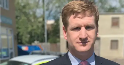 MATTHEW SCOTT/KENT PCC Matthew Scott is standing outside, next to a police car and there is also a police building seen over his shoulder.