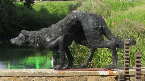 Bridport Town Council Side view of the black stalking dog sculpture on the wall above the river and weir.