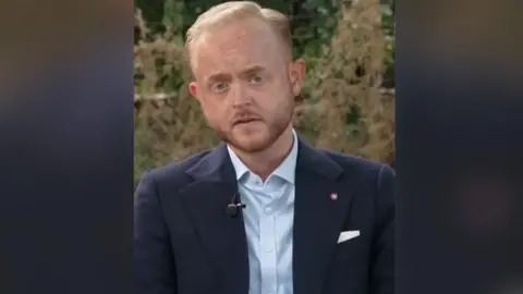 Man in navy suit and pale blue shirt sitting in park