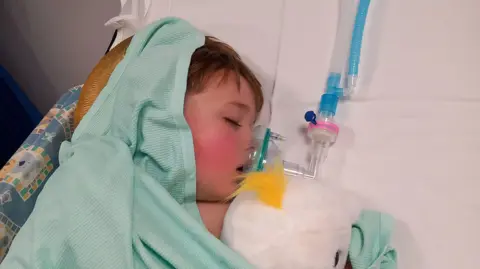 REBEKAH DALRYMPLE Hector in a hospital bed, he has a blue towel over his head and a plastic mask going to his mouth.