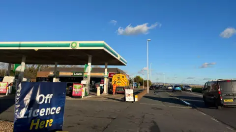 BBC/George Carden The forecourt of Brooklands Service Station in Worthing, showing petrol pumps and a shop, with an off licence sign