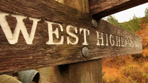 Getty Images A wooden sign on the West Highland Way directing people where to go. In white lettering the sign reads: "West Highland Way".