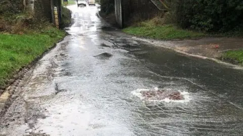 CDC A road blocked by floodwater and sewage. A van is driving through the water in the distance.