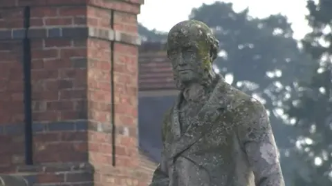 A weathered stone sculpture of a man wearing a heavy coat. 