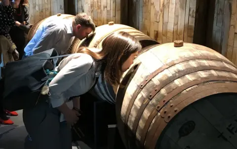 Visitors to a distillery sniffing a barrel of maturing whisky
