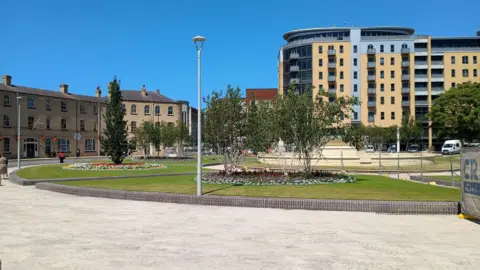 BBC / Ben Cook A view of the Rose Bowl and fountain in Hull as construction work takes place in Queen's Gardens, Hull. The cream coloured fountain stands in the centre of the image surrounded by a circular path and large, raised lawns and flower beds with trees. Construction fencing and vehicles are visible in the background.