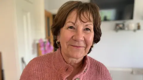 A woman with brown hair and pink cardigan
