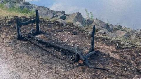 Charred remains of a wooden bench by a large lake