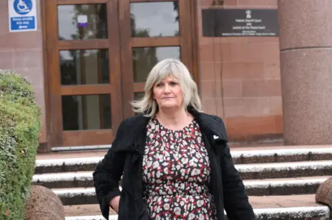 Central Scotland News Agency A pistillate   wearing a red, achromatic  and achromatic  dress, and a achromatic  overgarment   leaves a tribunal  building