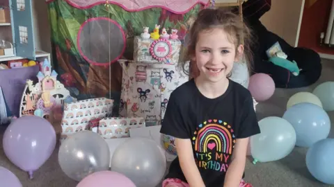 Family handout Jasmine, who has a stammer, smiling on her birthday in front of balloons and presents