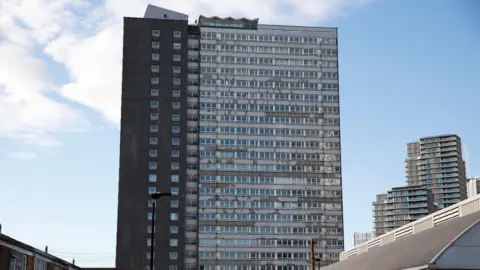 Dennison Point on the Carpenters Estate, a large pebble-dashed tower block looking fairly dilapidated with peeling paint on the outside of window frames