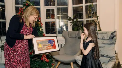 British Board of Film classification A woman is holding a copy of Ruby's painting signed by the cast of Sonic 3. Ruby is laughing